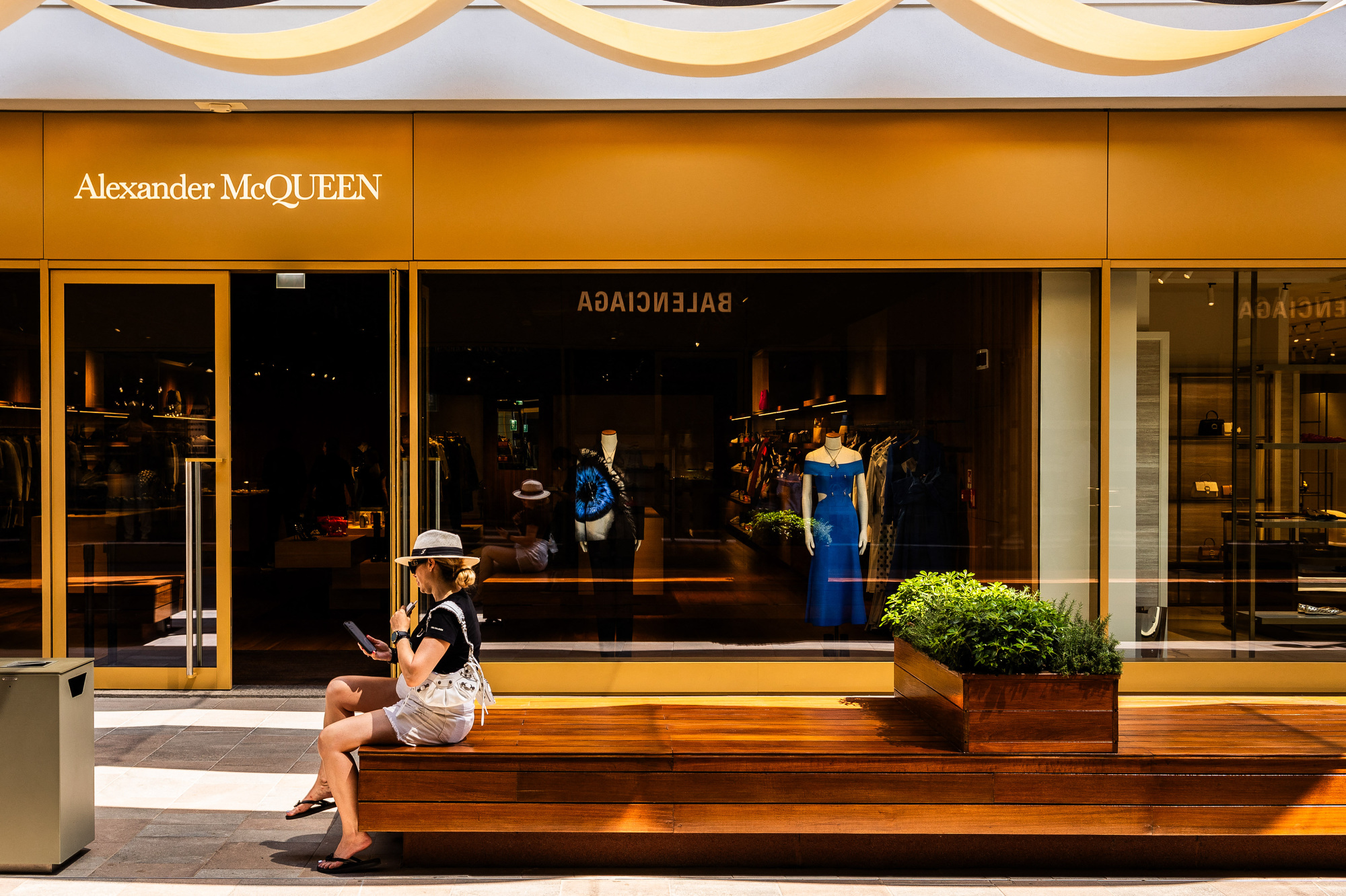 Woman on her telephone sitting in front of the Alexander McQueen boutique in The Mall Outlet on the outskirts of the town of Sanremo in Liguria, eastern Italy, July 31, 2024. (Photo by Jc Milhet / Hans Lucas / Hans Lucas via AFP) (Photo by JC MILHET/Hans Lucas/AFP via Getty Images)